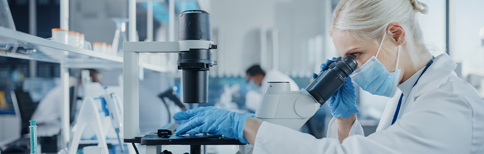 Frau im Labor schaut durch ein Mikroskop